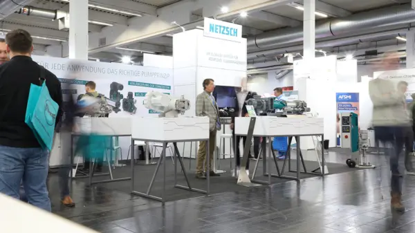 As bombas industriais da NETZSCH em exposição no estande de uma feira comercial, com visitantes e demonstrações de tecnologia.