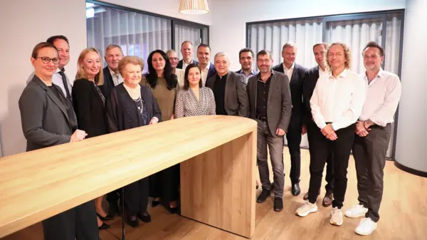 Groupe d'employés et de dirigeants de NETZSCH réunis autour d'une table en bois, célébrant le travail d'équipe et l'innovation dans un environnement de bureau moderne.