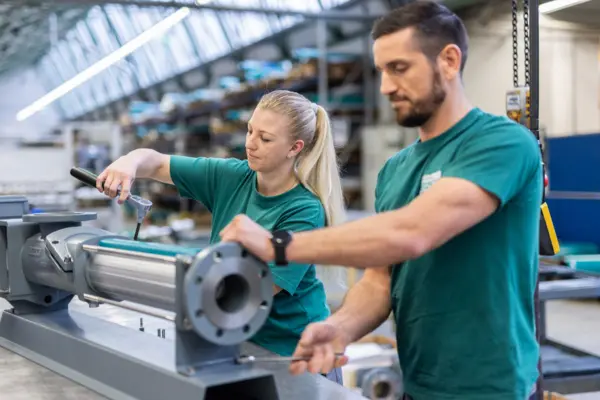 Dos técnicos ensamblan una bomba en un entorno industrial, mostrando concentración y colaboración.