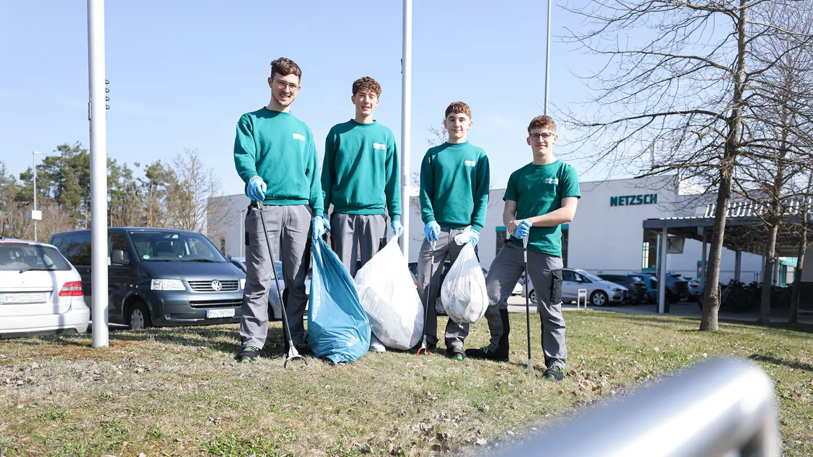 Four NETZSCH apprentices in green shirts and gray pants holding trash bags and litter pickers during a community cleanup event.