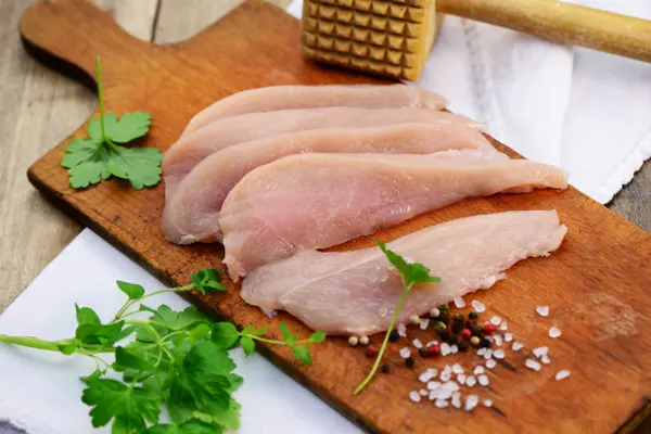 Raw turkey breast fillets on a wooden cutting board with fresh herbs, coarse salt, and pepper for poultry processing.