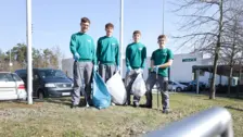 Cuatro aprendices de NETZSCH con camisas verdes y pantalones grises sostienen bolsas de basura y recogedores durante un evento de limpieza comunitaria.