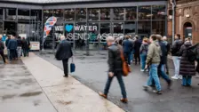 Visitors enter a modern building with large glass windows displaying "WE ♥ WATER TAUSENDWASSER" during a water industry event.
