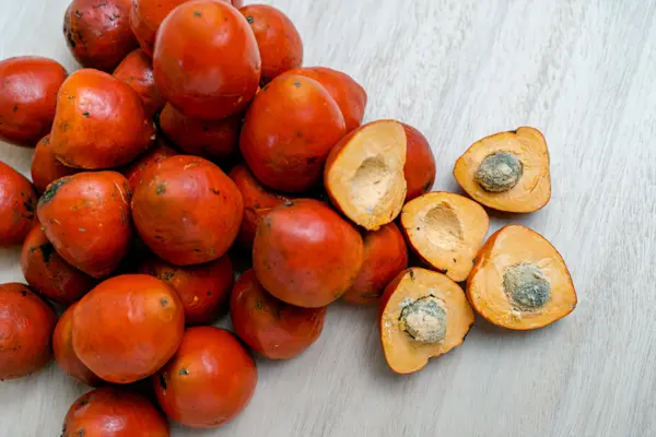 Close-up of palm oil fruit, showcasing vibrant red skin and split specimens revealing the inner seed, highlighting palm oil production's natural sources.