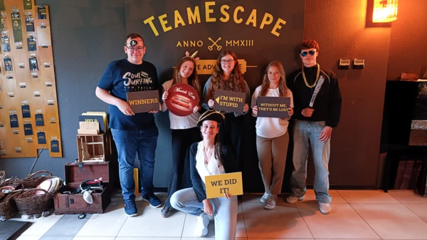 Trainees celebrate their escape room success, holding playful signs reflecting teamwork and fun in Stuttgart.