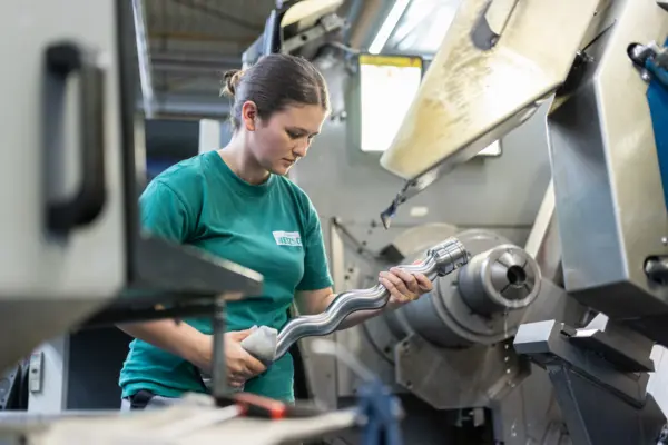 Mujer en una máquina trabajando con una pieza de bomba, luciendo concentrada en un entorno industrial.
