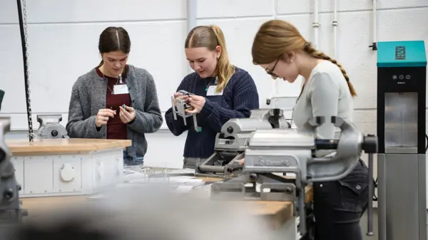 Jonge vrouwen doen mee aan een praktische technische training in de NETZSCH workshop om hun vaardigheden in MINT-beroepen te verbeteren.