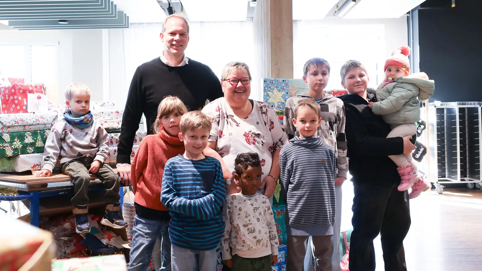 Enfants et adultes rassemblés autour d'un arbre de Noël décoré, souriant lors de la distribution de cadeaux, répandant la joie de Noël chez NETZSCH.