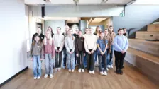Grupo de mujeres jóvenes y niñas de pie en un moderno espacio de oficinas para el evento del Día de las Niñas NETZSCH que promueve la diversidad y la innovación.