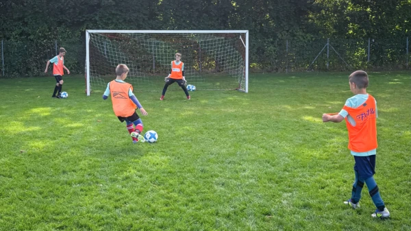 Bambini in maglia arancione si esercitano a giocare a calcio durante un campo di calcio inclusivo, promuovendo il lavoro di squadra e la comunità.