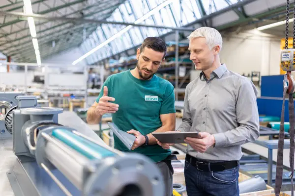 Zwei Männer besprechen NETZSCH Ersatzteile in moderner Fabrikumgebung, Fokus auf technische Beratung und Pumpenservice.