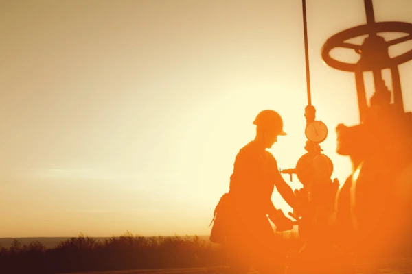 Ein Arbeiter in Schutzkleidung bedient eine Pumpe im Öl- und Gasbereich bei Sonnenuntergang. Sicherheit und Präzision stehen im Fokus.