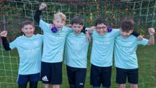 Five children in "Kick & Fun" jerseys celebrate together in front of a soccer goal, showcasing teamwork and joy in sports.