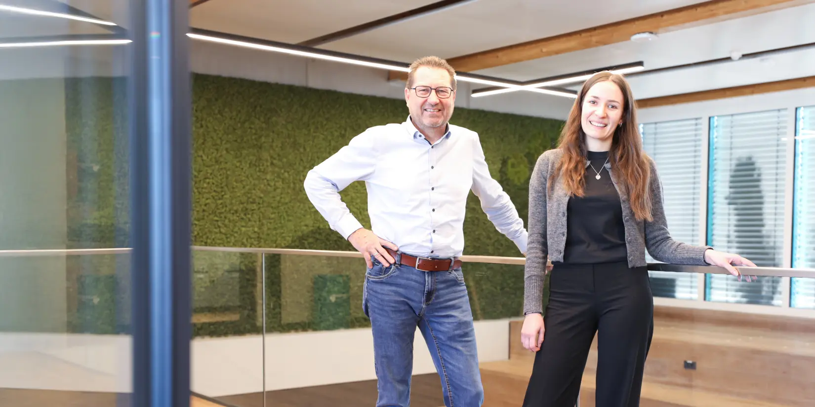 Nina Schwalm und Johann Vetter standen lächelnd in einem modernen, umweltfreundlichen Büroraum mit Holz- und Grünelementen, die die Nachhaltigkeit bei NETZSCH unterstreichen.