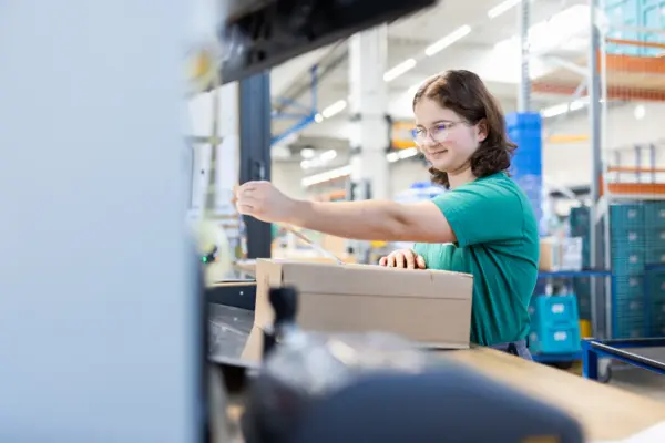Mädchen verpackt Karton im Lager, effiziente Logistikprozesse für Ersatzteile bei NETZSCH Pumpen & Systeme.