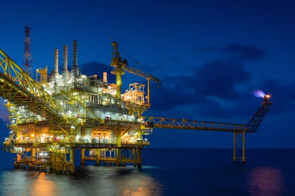 Ölplattform bei Nacht mit leuchtenden Strukturen und Versorgungspipeline, Symbol für innovative Pumpenlösungen im Öl- und Gasbereich.