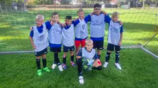 Sieben Kinder in blau-weißen Trikots posieren lachend vor einem Fußballtor auf grünem Rasen beim integrativen Kick & Fun Fußballcamp.