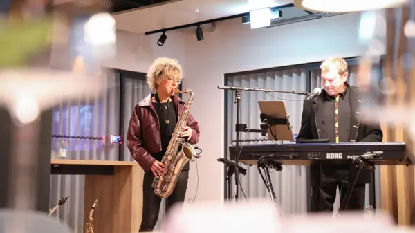 Un saxophoniste joue sur scène aux côtés d'un claviériste lors d'un événement festif chez NETZSCH, créant ainsi une atmosphère animée pour les participants.