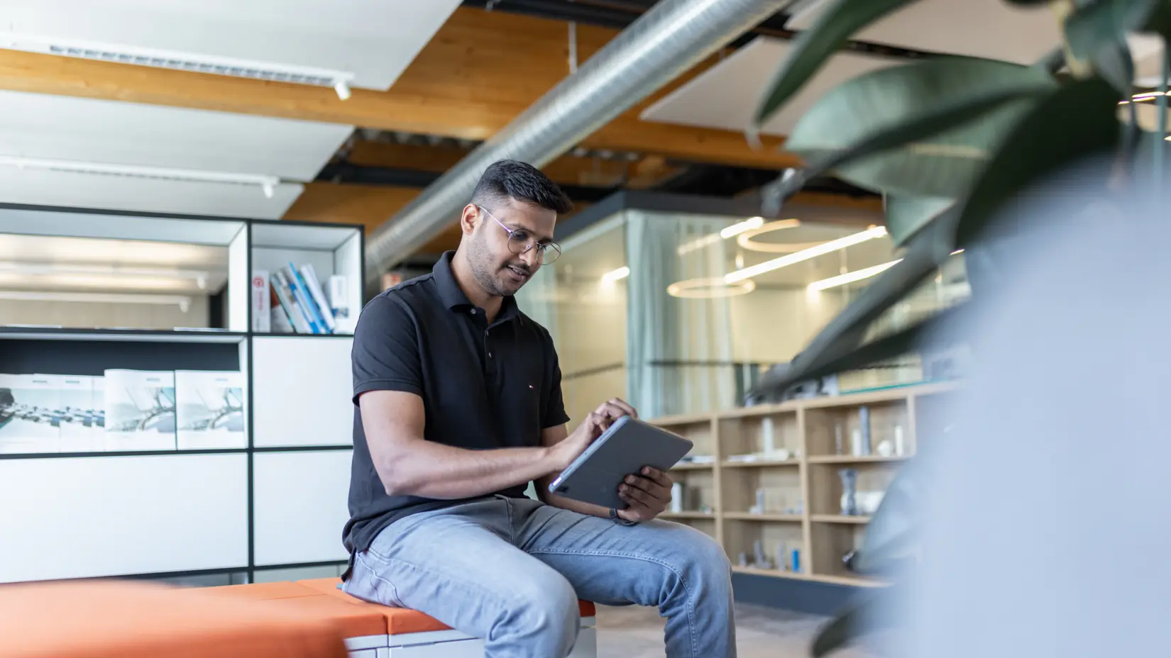 Man in black polo using tablet in modern office, focused on digital consultation and technical planning.
