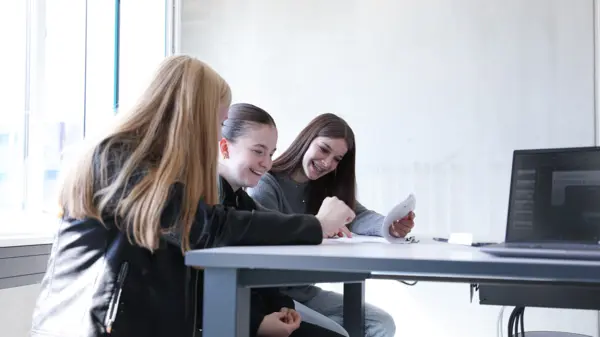 Three young women engaged in a collaborative discussion, reviewing documents and smiling during a technical apprenticeship session at NETZSCH.