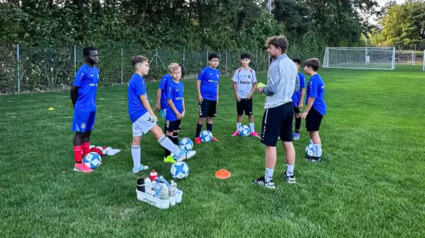 Youth football coach instructing a diverse group of kids in blue jerseys at inclusive Kick & Fun camp in Waldkraiburg.
