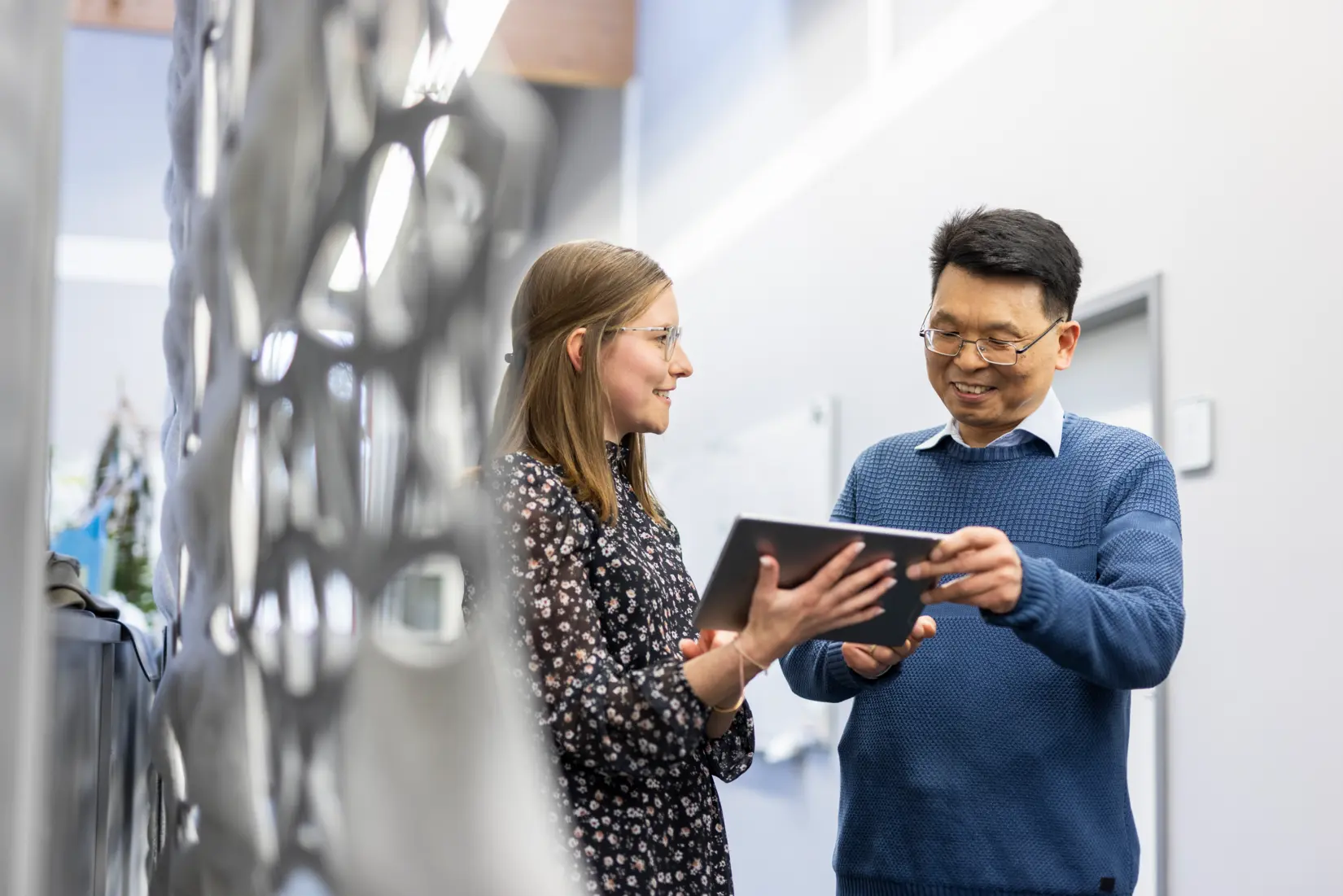 A man and woman engage in a collaborative discussion while reviewing a tablet, showcasing teamwork in a professional setting.