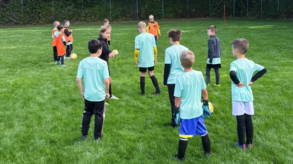 Bambini in maglia azzurra si allenano a calcio su un campo verde, promuovendo il lavoro di squadra e l'inclusività in un campo giovanile.