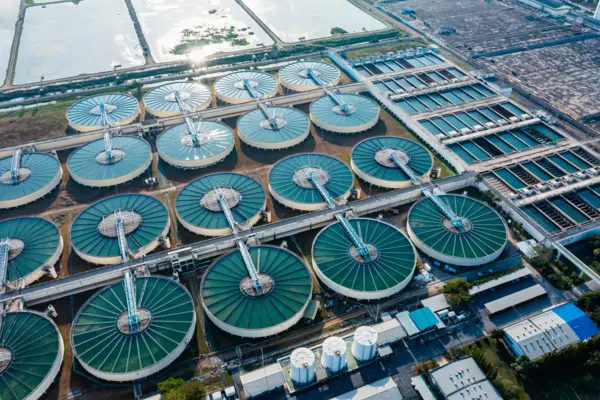 Aerial view of a large wastewater treatment plant featuring multiple circular membrane filtration tanks with rotating mechanisms under clear daylight.