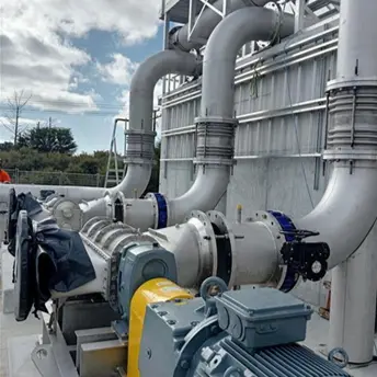 Industrial reversible rotary lobe pump system with large metal pipes in a wastewater treatment plant under a blue sky.